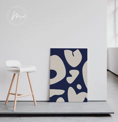 an abstract painting on the wall next to a white chair and stool in a room