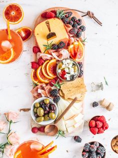 an assortment of fruits and cheeses on a platter with orange slices, olives, strawberries