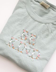 an embroidered t - shirt with flowers on the front and back, sitting on a white surface