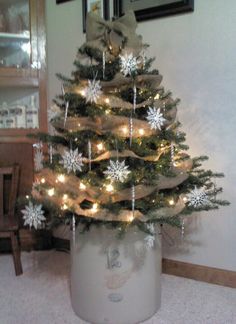 a small christmas tree in a white container with lights on the top and snowflakes hanging from it