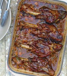 a casserole dish with meat in it on a table next to silverware