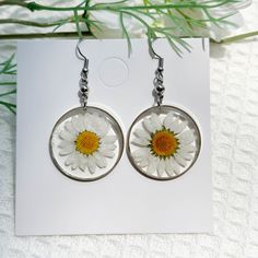 a pair of dandelion earrings sitting on top of a piece of white paper