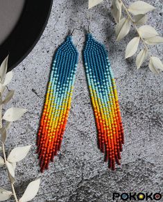 two pairs of multicolored beaded earrings on top of a table next to leaves