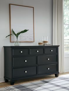 a black dresser sitting in front of a window next to a painting on the wall