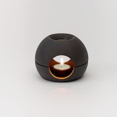 a small black candle holder with a lit candle in it's center on a white surface