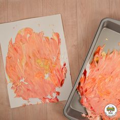 an art project with orange and white paint on paper next to a metal pan filled with watercolors