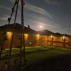 the sun is setting behind a fence with lights on in the dark sky above it