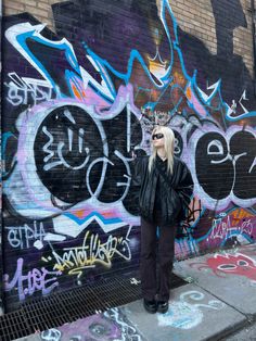 a woman standing in front of a wall with graffiti on it's sides and wearing sunglasses