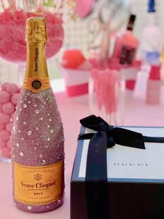 a bottle of champagne next to a gift box and some pink candies on a table