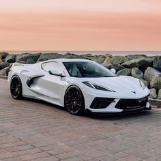 a white sports car parked on the side of a road next to rocks and water