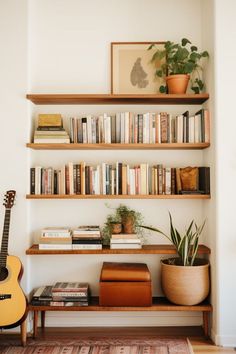 a bookshelf filled with lots of books next to a guitar and potted plant