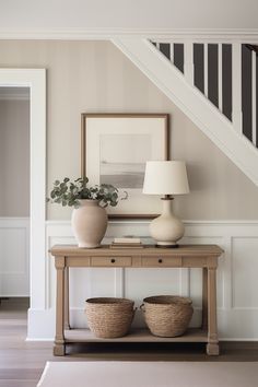 a table with two baskets under a stair case next to a lamp and pictures on the wall