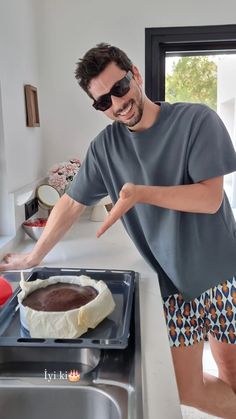 a man wearing sunglasses pointing at a cake in a pan on the kitchen counter top