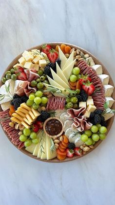 a platter filled with different types of cheeses and fruits on a marble surface