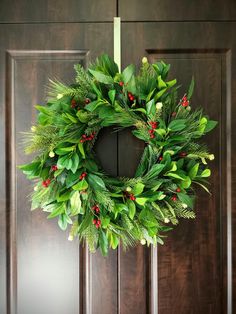 a wreath hanging on the front door of a house with greenery and red berries