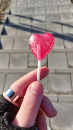 a person holding a heart shaped lollipop on a stick