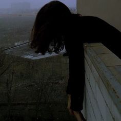 a woman leaning on the side of a building with her head down, in front of an overcast sky