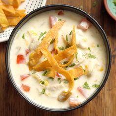 a bowl filled with soup and chips on top of a wooden table next to a plate