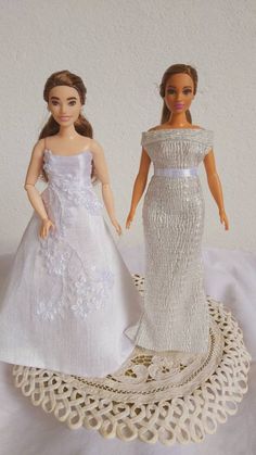 two barbie dolls in wedding dresses on a doily with white wall and floor behind them