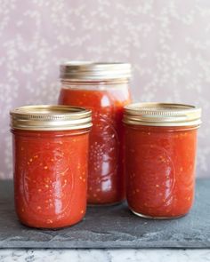 three jars filled with tomato sauce sitting on top of a counter