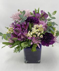 a vase filled with purple flowers and greenery