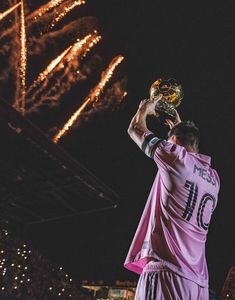 a man holding up a soccer ball in front of fireworks