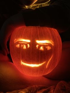 a pumpkin carved to look like a face with glowing eyes and mouth is being held by someone's hand