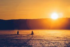 the sun is setting over some water with people on skis