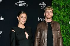 a man and woman standing next to each other in front of a green plant wall