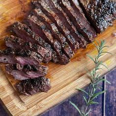 steak sliced up on a wooden cutting board with rosemary sprig next to it