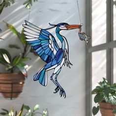 a stained glass bird ornament hanging from a window with potted plants in the background