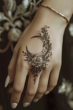 a woman's hand with a crescent and flowers tattoo on the ring finger is shown