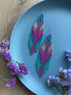 two pink and blue beaded earrings on a plate next to purple flowers