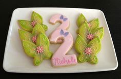 decorated cookies on a white plate with pink and blue butterflies, the number two is made out of icing