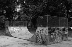 black and white photograph of skateboard ramps with graffiti on the walls in a park