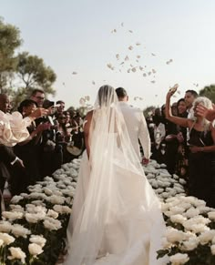 the bride and groom are walking down the aisle with their guests throwing petals in the air