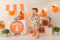 a baby girl standing in front of an orange themed backdrop and eating something with her hands