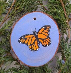 an orange butterfly painted on a piece of wood sitting on top of some green branches