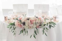 the table is set with white chairs and floral centerpieces on top of it