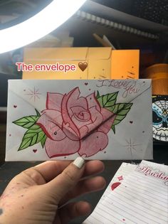 a hand holding an envelope with a rose on it and the envelope has been drawn