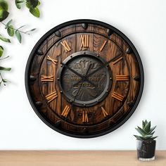 a wooden clock with roman numerals on the face next to a potted plant