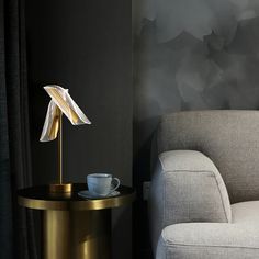 a white couch sitting next to a table with a cup on it and a lamp