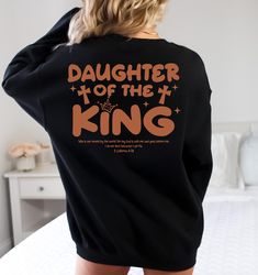 Daughter Of The King Shirt, Aesthetic Christian Sweatshirt, Women's Religious Hoodie, Bible Verse Shirt, Christian Gifts, Church Shirt,R248 ♥️ WELCOME ♥️ Looking for super soft, comfy, and high-quality clothes for your special days or loved ones? You've come to the right place! We absolutely love what we do and are dedicated to making your shopping experience just perfect. If you have any questions about our products, don't hesitate to reach out. We're here to help and will get back to you as soon as possible! 🔵 HOW TO ORDER  1️⃣Select the t-shirt size 2️⃣ Select the color 3️⃣ If you have, add your personalized designs, enter customization in "Add your personalization" field 4️⃣ Add to cart 5️⃣ Go back and Repeat for each size (to create a set ) ♻️ CARE INSTRUCTIONS  🟢 Wash item inside o Black Relaxed Fit Hoodie, Pre-shrunk, Casual Hoodie Tops With Custom Print, Relaxed Fit Slogan Hoodie, Band Merch Long Sleeve Sweatshirt With Custom Print, Relaxed Fit Hoodie With Slogan, Pre-shrunk Relaxed Fit Hoodie, Fall Letter Print Hooded T-shirt, Fall Hooded T-shirt With Letter Print, Comfortable Fit Long Sleeve Hoodie With Graphic Print