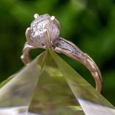 a diamond ring sitting on top of a green piece of glass with leaves in the background