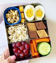 a lunch box filled with crackers, grapes, cucumber, carrots and hard boiled eggs