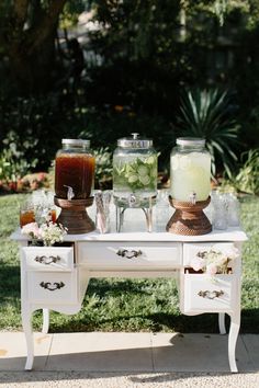 a white table topped with jars filled with liquid and flowers sitting on top of a grass covered field