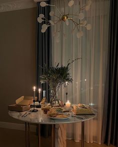 a table that has some food on it and candles in front of the window with curtains