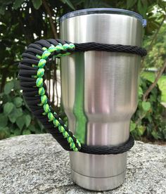 a stainless steel cup sitting on top of a rock next to a green and black rope