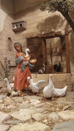 a figurine of a woman feeding ducks in front of a brick wall and tree