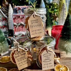 three jars filled with oranges and spices on top of a wooden table next to christmas trees